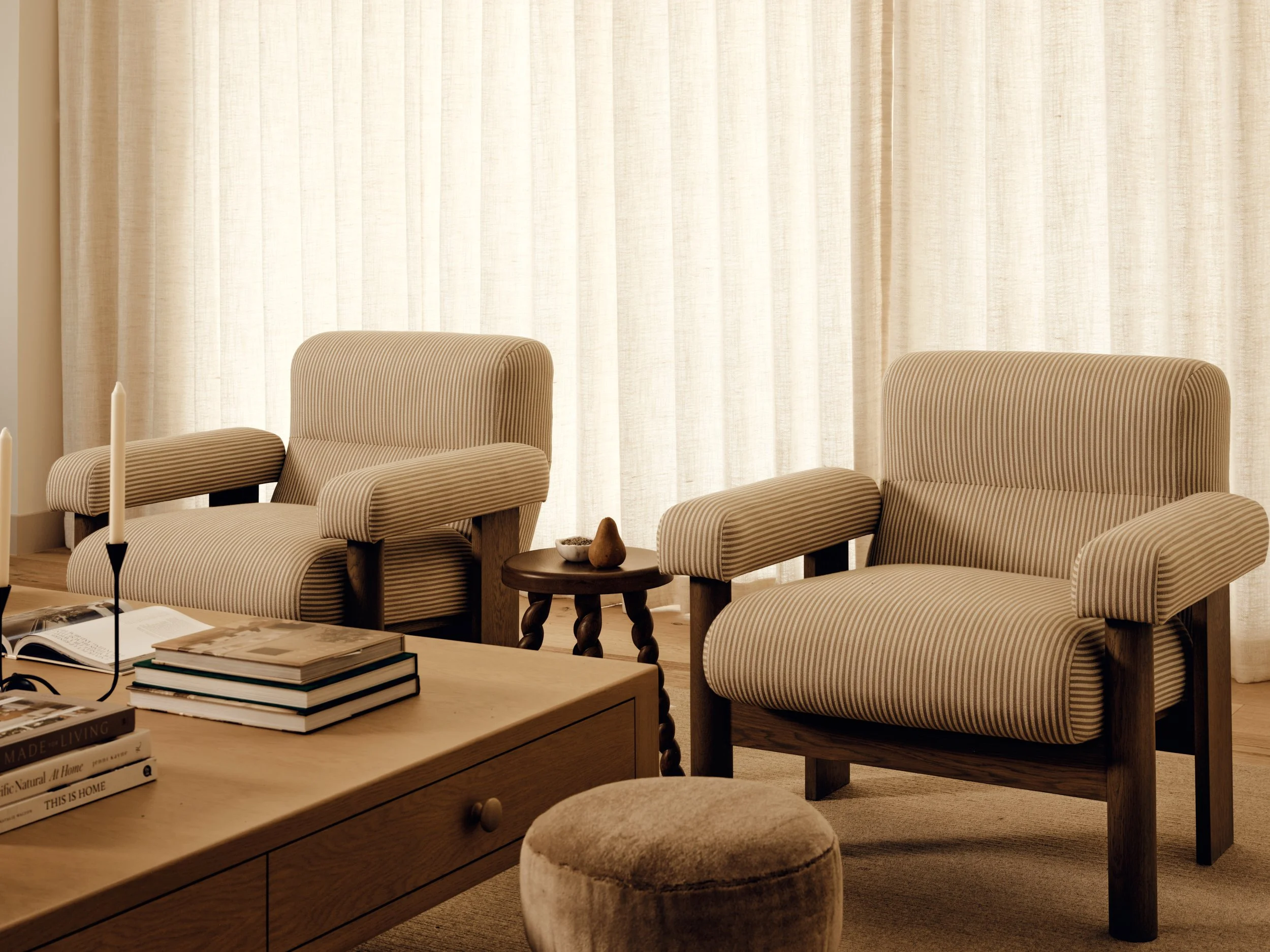 Organic modern living space with striped accent chairs, boucle ottomans, and soft drapery